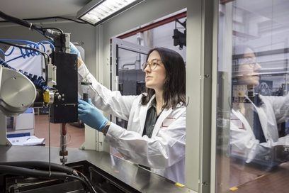 Eine Frau arbeitet mit Handschuhen an einem industriellen 3D-Drucker.
