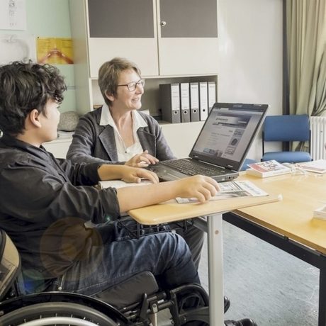 Eine Lehrerin erklärt einem Jungen im Rollstuhl etwas am Computer. (Foto: Bundesagentur für Arbeit)