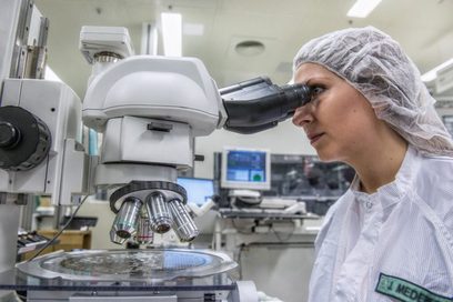 Junge Frau schaut durch ein Mikroskop auf einen Wafer