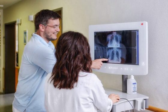 Junger Mann sichtet gemeinsam mit einer Ärztin an einem Computer auf dem Gang ein Krankenhauses ein Röntgenbild. (Foto: Julien Fertl)