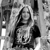 Schwarzweiß-Bild der Restaurierungs-Studentin Lis Mette Eggers, die vor einem alten Metallbauwerk steht und zur Kamera sieht. 