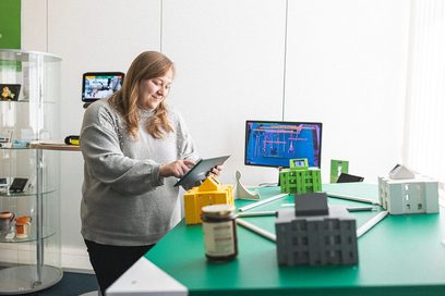 Christina Erler steht vor einem Blockchain-Demonstrator und hält ein Tablet in der Hand, womit sie die Anwendung bedienen kann.