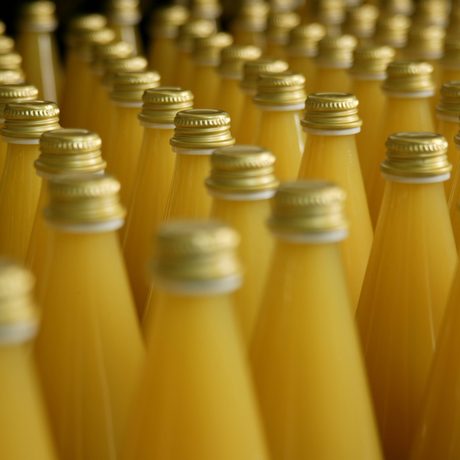 Detail: Viele Glasflaschen ohne Aufschrift und mit einem goldenen Deckel, die Orangensaft enthalten sind aneinandergereiht. 