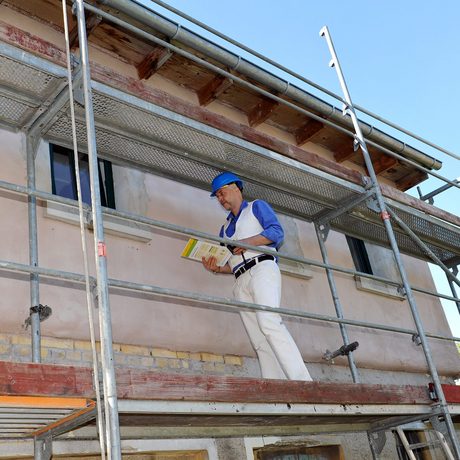 Ein Bauarbeiter steht auf einem Gerüst an einer Hauswand.