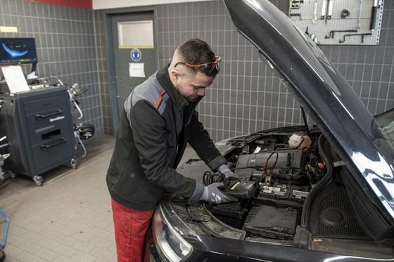 Ein junger KFz-Mechatroniker überprüft die Leistung einer Autobatterie.