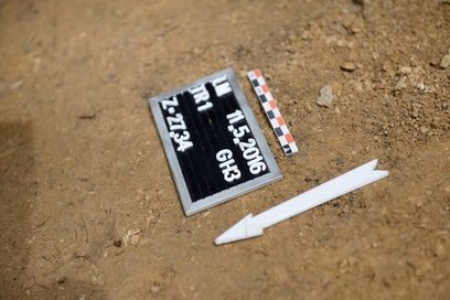 Detailaufnahme von einem Fundstück mit einer Tafel mit den Funddaten in einer Grabungsstätte.