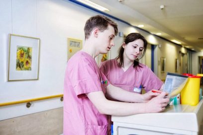 Zwei junge Krankenpfleger stehen im Krankenhausflur und besprechen sich.