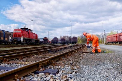 Foto einer Eisenbahnerin im Betriebsdienst vor einem Bahngleis.