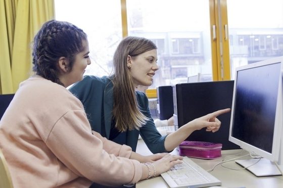 Eine junge Frau zeigt einer anderen jungen Frau etwas am Computer.