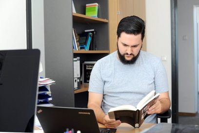 Ein Mann sitzt an einem Schreibtisch und liest in einem Fachbuch.