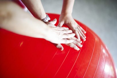 Eine Physiotherapeutische Situation: vier Hände, die auf einen roten Ball drücken