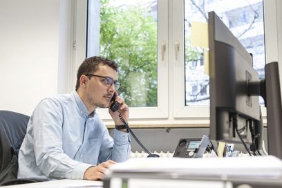 Ein Mann sitzt im Büro am Computer und telefoniert.