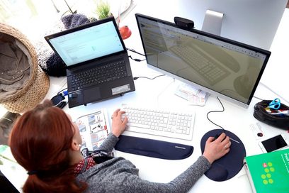 Junge Frau arbeitet an einem Schreibtisch an zwei Bildschirmen.  (Foto: Martin Rehm)