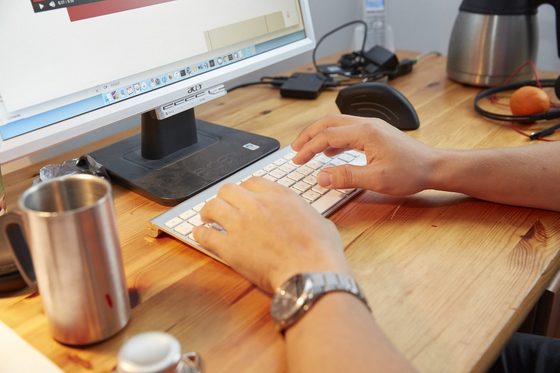 Ein Mann sitzt in einem Büro am Schreibtisch und arbeitet mit Computer und Headset.