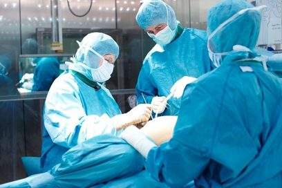 Drei Ärzt*innen in blauer Kleidung stehen um einen OP-Tisch und führen einen Eingriff durch. (Foto: Tilman Weishart)