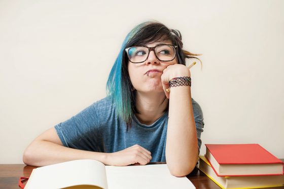 Junge Frau sitzt gelangweilt vor ihren Büchern und verdreht die Augen.
