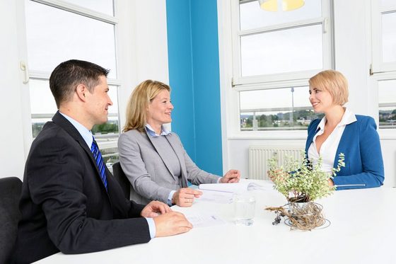 Ein Mann und zwei Frauen sitzen am Tisch in einem Meetingraum und unterhalten sich.