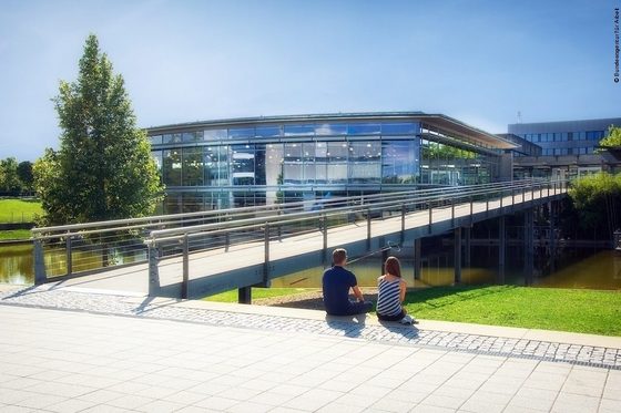 Zwei Personen sitzen neben einer Brücke auf dem Campus der Hochschule Regensburg.