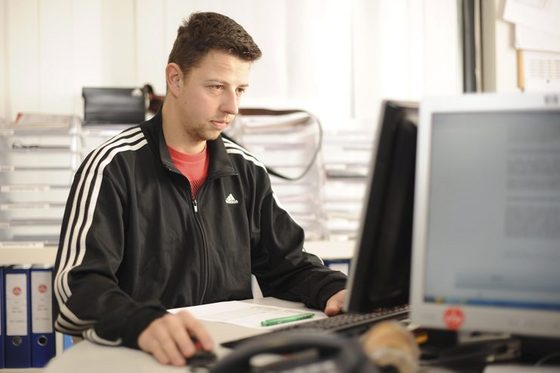 Das Foto zeigt einen jungen Mann vor dem PC, der sportlich gekleidet ist.
