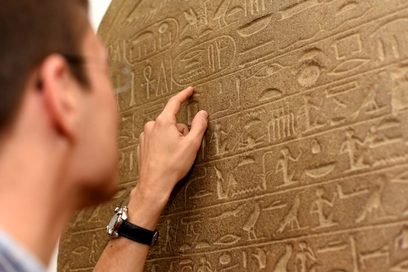 Ein Mann liest ägyptische Schriftzeichen auf einer Steinwand.