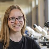 Biotechnologie-Studentin Ronja Tittel steht in einem Labor und blickt in die Kamera. 