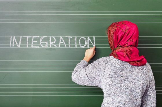 Eine Frau mit Kopftuch schreibt "Integration" an eine Schultafel