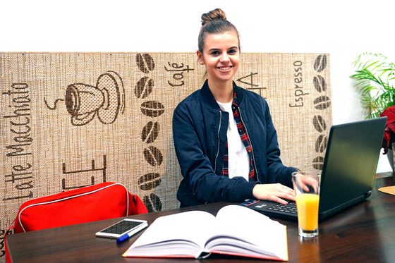 Eine Studentin sitzt vor Ihrem Laptop in einem Cafe.