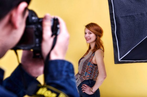 Junge Frau steht vor gelbem Hintergrund in einem Studio und wird fotografiert