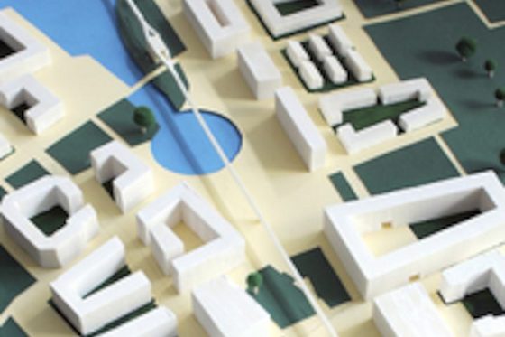 Detailaufnahme von einem dreidimensionalen Modell einer Stadtplanung, auf dem Gebäude, ein Gewässer und Grünflächen zu sehen sind.