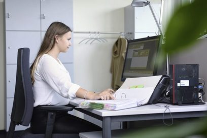 Eine junge Frau überprüft abgelegte Daten im Ordner und am Computer.