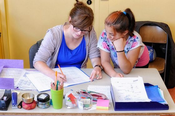 Ein Foto von einer Lehrerin neben einer Schülerin. Sie arbeiten gemeinsam an Lernmaterial.