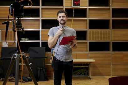 Ein junger Mann steht mit Klemmbrett und Ohrstecker in einem Filmstudio.