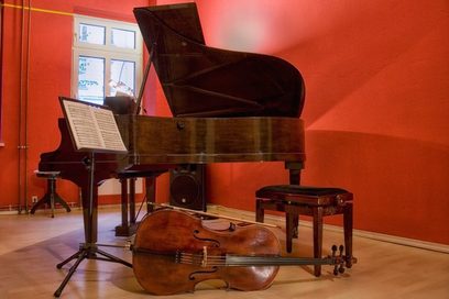 Zu sehen ist ein rot gestrichener Raum mit einem Flügel, davor stehen ein Notenpult und ein Klavierhocker, im Vordergrund liegt ein Cello. (Foto: Sonja Trabandt)