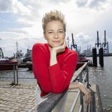 Susan M. steht in einem Hafen an ein Geländer gelehnt und blickt in die Kamera.