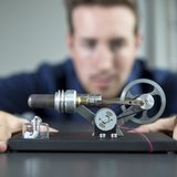 Nahaufnahme eines Stirlingmotors, der im Hintergrund von einem Student geprüft wird (Foto: Axel Jusseit)