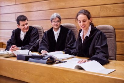 Eine junge Frau in einer Richterrobe bespricht sich mit zwei Kollegen in einem Verhandlungssaal