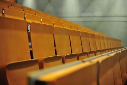 Leere Sitzreihen in einem Hörsaal, angeordnet als Tribüne. Die Wandrückseite ist eine Sichtbetonwand .