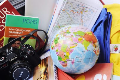 Gegenstände, die mit einer Auslandsreise assoziiert sind, wie ein Globus, eine Kamera und eine Landkarte.