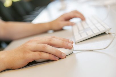 Hände tippen auf einer weißen Tastatur und umfassen eine weiße Computermaus.