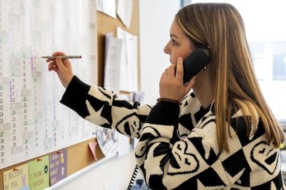 Eine junge Frau trägt einen Termin im Wandkalender ein, während sie telefoniert.