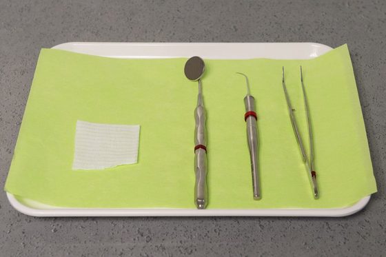 Zahnmedizinisches Besteck liegt auf einem weißen Tablett mit grünem Tuch.