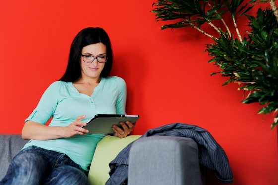 Eine Frau mit Brille lsitzt auf einem Sofa und blickt auf ein Tablet. (Foto: Julien Fertl)