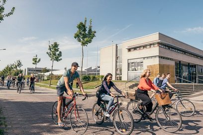 Imagebild (Pressefoto) der Hochschule Stralsund: Studierende radeln über den Campus, im Hintergrund ein Campusgebäude.