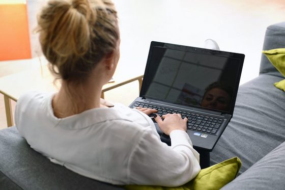 Eine junge Frau sitzt auf einer Couch und arbeitet an ihrem Laptop.