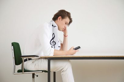 Ein junger Mann sitzt an einem Tisch und tippt etwas in sein Handy.