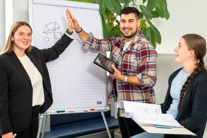 Zwei junge Frauen und ein junger Mann feiern Erfolg mit Abklatschen.