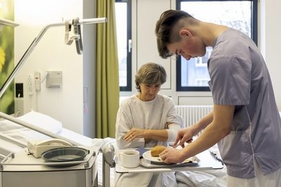 Ein Krankenpfleger schmiert ein Brot für eine Patientin.