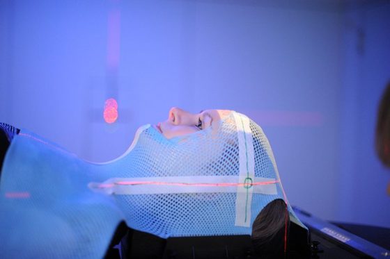 Junge Frau mit Maske auf dem Kopf bei einer Strahlentherapie.
