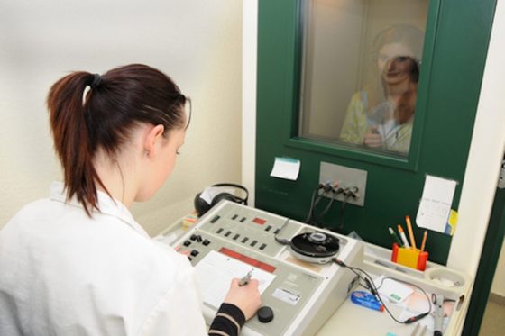 Eine junge Frau im Kittel protokolliert die Daten eines Hörtestes mit dem Audiometer.