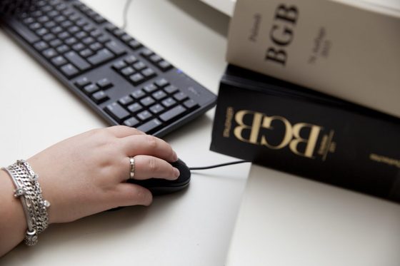 Eine Hand bedient eine Computermaus. Daneben liegen Gesetzbücher. (Foto: Julien Fertl | Bundesagentur für Arbeit)
